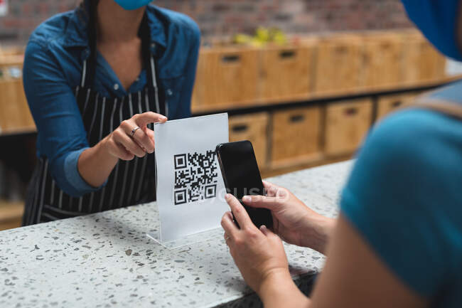 Midsection of two caucasian women one taking picture of qr code over counter. fitness and leisure time at gym during coronavirus covid 19 pandemic. — Stock Photo
