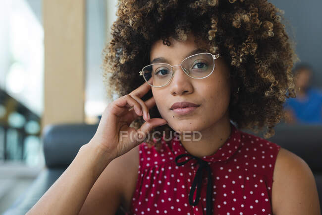 Portrait of mixed race businesswoman wearing glasses sitting on sofa. casual meeting in business lounge. — Stock Photo