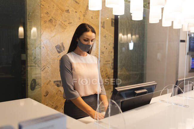 Retrato de mujer caucásica con máscara facial trabajando en recepción en hotel. viaje de negocios hotel durante coronavirus covid 19 pandemia. - foto de stock