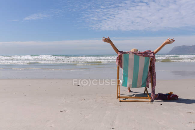 Кавказька жінка в бікіні сидить на палубному стільці на пляжі. Здоровий вільний час на відкритому повітрі біля моря. — стокове фото