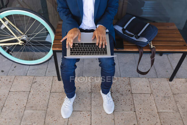 Seção média do macho sentado no banco na rua usando laptop. nômade digital, para fora e sobre na cidade. — Fotografia de Stock