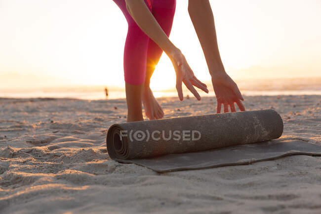 Metà sezione di donna rotolamento tappetino yoga in spiaggia. fitness yoga e stile di vita sano concetto — Foto stock