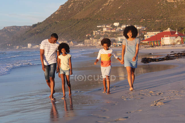Smiling african american parents and two children walking and holding hands at the beach. family outdoor leisure time by the sea. — Stock Photo