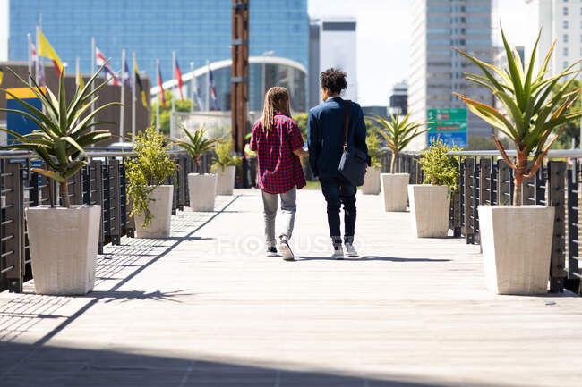 Двое друзей смешанной расы идут по улице и разговаривают. зеленый городской образ жизни, вне и около в городе. — стоковое фото