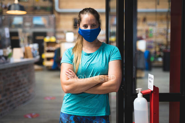Portrait of caucasian woman wearing mask standing in corridor at gym. fitness and leisure time at gym during coronavirus covid 19 pandemic. — Stock Photo
