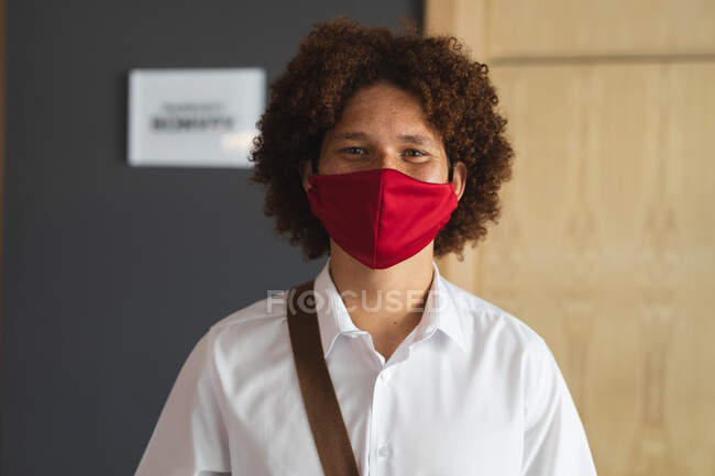 Portrait of mixed race man wearing face mask standing in hotel lobby with shoulder bag. business travel hotel during coronavirus covid 19 pandemic. — Stock Photo
