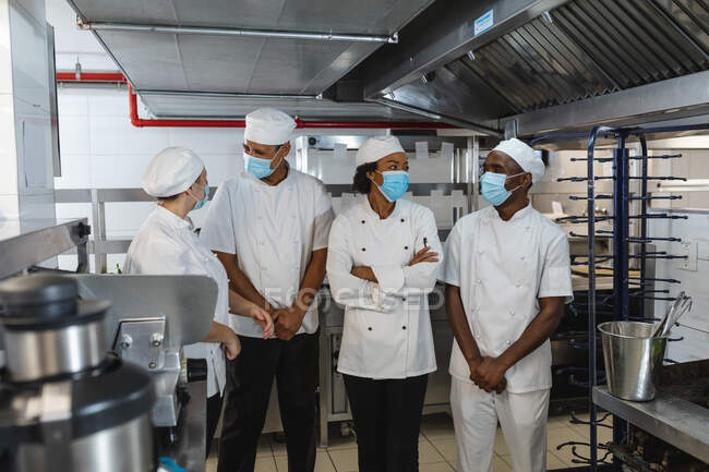 Portrait of diverse race male and female professional chefs standing in face masks. working in a busy restaurant kitchen during coronavirus covid 19 pandemic. — Stock Photo