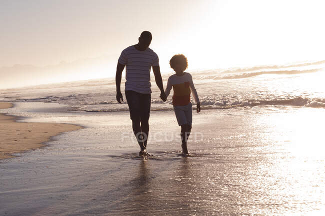 African american father and daughter walking and holding hands at the beach. family outdoor leisure time by the sea. — Stock Photo