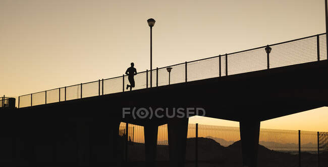 Uomo afroamericano che si allena all'aperto correndo sul ponte al tramonto. sano stile di vita all'aperto allenamento fitness. — Foto stock
