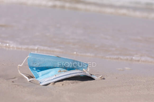 Face mask lying in sand on a beach. healthy outdoor leisure time by the sea during coronavirus covid 19 pandemic. — Stock Photo
