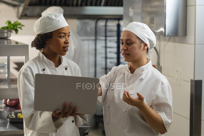 Ritratto di diversi chef professionisti di razza femminile che discutono su laptop. lavorando in una cucina ristorante occupato. — Foto stock