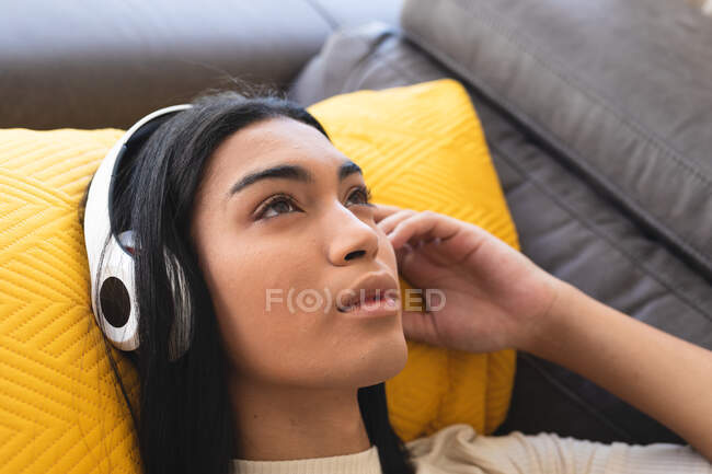 Mujer transexual de raza mixta feliz relajarse en la sala de estar tumbado en el sofá con auriculares. permanecer en casa aislado durante el bloqueo de cuarentena. - foto de stock