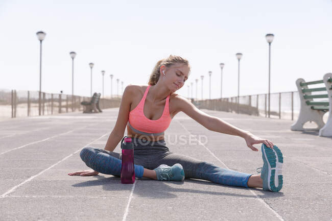 Caucasian woman exercising stretching on a promenade by the beach. healthy outdoor leisure time by the sea. — Stock Photo