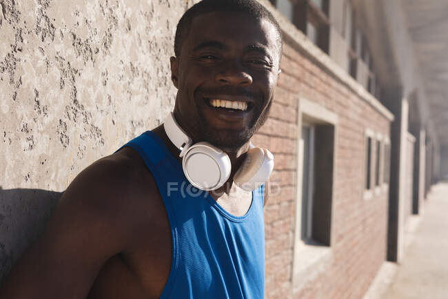 Portrait of smiling african american man exercising outdoors, wearing headphones. healthy outdoor lifestyle fitness training. - foto de stock