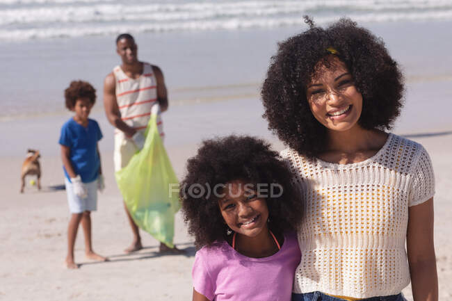 Африканские американские родители с двумя детьми собирают мусор с пляжа улыбаясь. сохранение семейного экологического пляжа. — стоковое фото