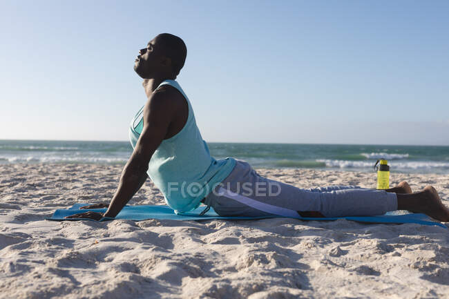 Entspannter afrikanisch-amerikanischer Mann, der im Freien trainiert und Yoga am Strand praktiziert. gesundes Outdoor-Fitness-Training. — Stockfoto