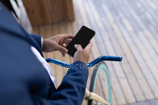 Средняя часть смешанной расы мужчины с велосипедом с помощью смартфона на улице. цифровая реклама, наружная и по городу. — стоковое фото
