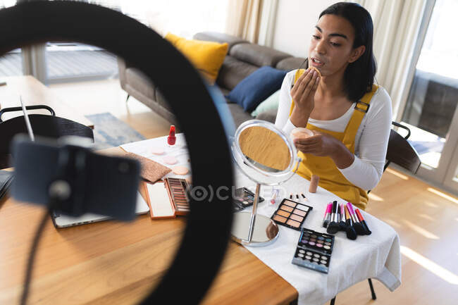 Mulher transgênero de raça mista fazendo vlog usando laptop, smartphone e iluminação colocando maquiagem. ficar em casa em isolamento durante o confinamento de quarentena. — Fotografia de Stock