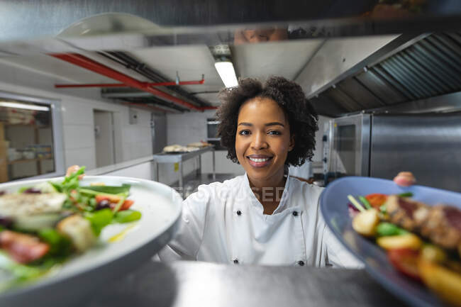 Mixed race professional chef giving away dishes to be served. working in a busy restaurant kitchen. — Stock Photo