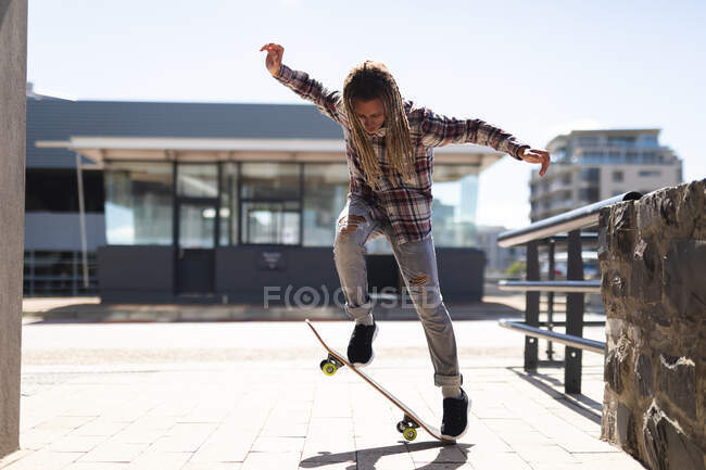 Maschio razza mista con dreadlocks skateboard in strada. stile di vita urbano verde, in giro per la città. — Foto stock