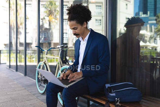 Maschio razza mista con baffi seduti sulla panchina in strada utilizzando il computer portatile. nomade digitale, in giro per la città. — Foto stock