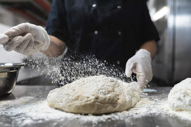 Средняя часть профессионального шеф-повара готовит тесто в гигиенических перчатках. работа на кухне ресторана. — стоковое фото