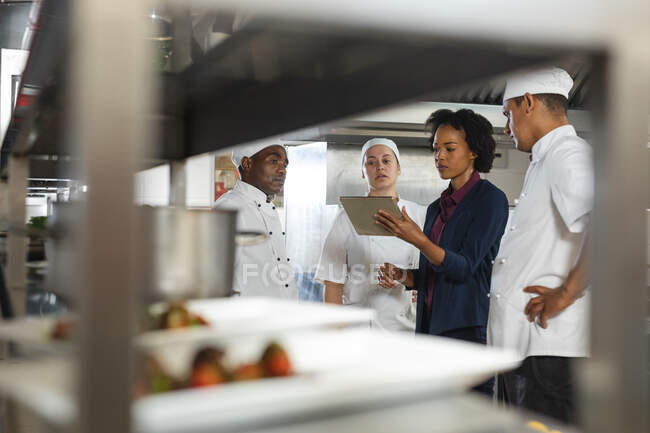 Diverso grupo de chefs profesionales que se reúnen con el gerente de cocina. trabajando en una cocina ajetreada. - foto de stock