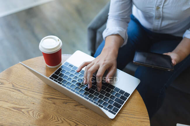 Sezione centrale della donna d'affari seduta nell'atrio che lavora al computer portatile che prende un caffè. viaggi d'affari settore alberghiero. — Foto stock