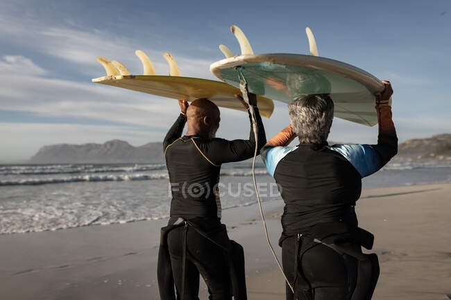 Ein älteres afrikanisch-amerikanisches Paar trägt am Strand ein Surfbrett auf dem Kopf. Reise Urlaub Ruhestand Lifestylekonzept — Stockfoto