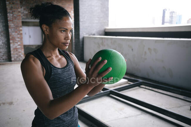 Mujer afroamericana en forma determinada ejercitando la celebración de la pelota de voleibol en el espacio vacío del almacén. fitness urbano y deporte. - foto de stock