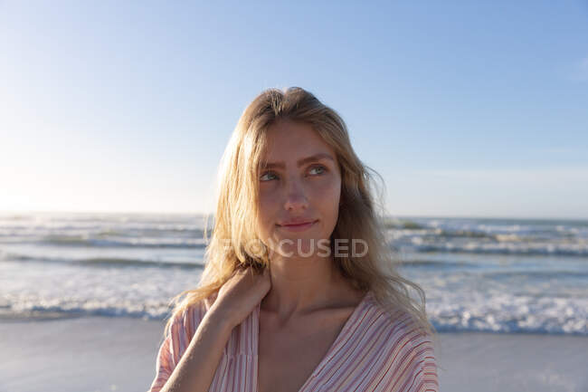 Caucasian woman wearing beach cover up touching her shoulder at the beach. healthy outdoor leisure time by the sea. — Stock Photo