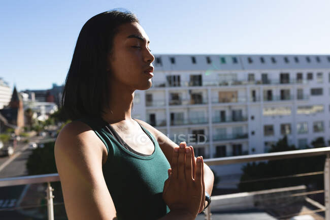 Женщина-трансгендер смешанной расы практикует медитацию йоги на террасе на крыше под солнцем. оставаться дома в изоляции во время карантинной изоляции. — стоковое фото
