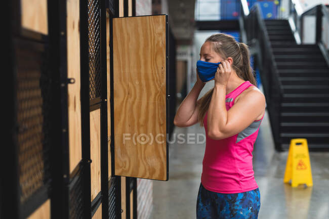 Caucasian woman standing by lockers and putting face mask on. fitness and leisure time at gym during coronavirus covid 19 pandemic. — Stock Photo