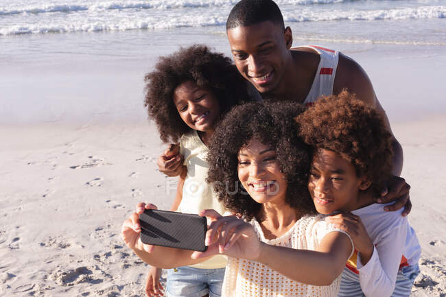 Afrikanische Eltern und zwei Kinder machen lächelnd ein Selfie mit dem Smartphone am Strand. Familienfreizeit im Freien am Meer. — Stockfoto