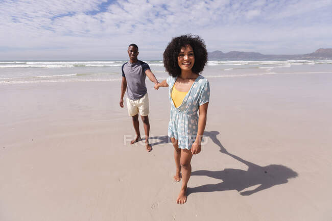 Африканская американская пара, идущая и держащаяся за руки на пляже, улыбается. здоровый отдых на открытом воздухе у моря. — стоковое фото