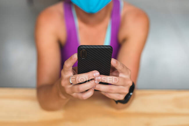 Sección media de una mujer caucásica que usa máscara usando un teléfono inteligente en la pared de escalada interior. fitness y tiempo libre en el gimnasio durante coronavirus covid 19 pandemia. - foto de stock