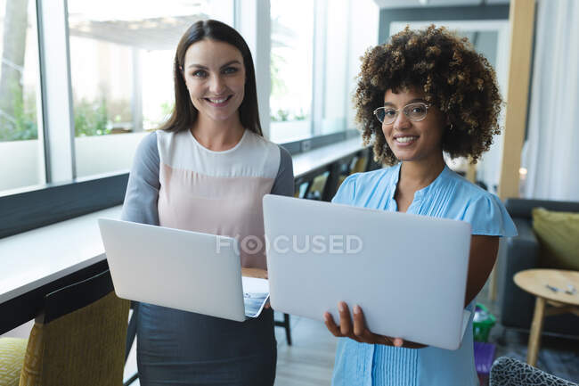 Портрет разнообразной женщины улыбающихся деловых коллег, стоящих с ноутбуками. Случайные встречи в бизнес-кругах. — стоковое фото