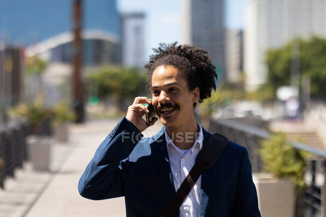 Feliz homem de raça mista inteligentemente vestido com bigode falando no smartphone na rua. nômade digital, para fora e sobre na cidade. — Fotografia de Stock