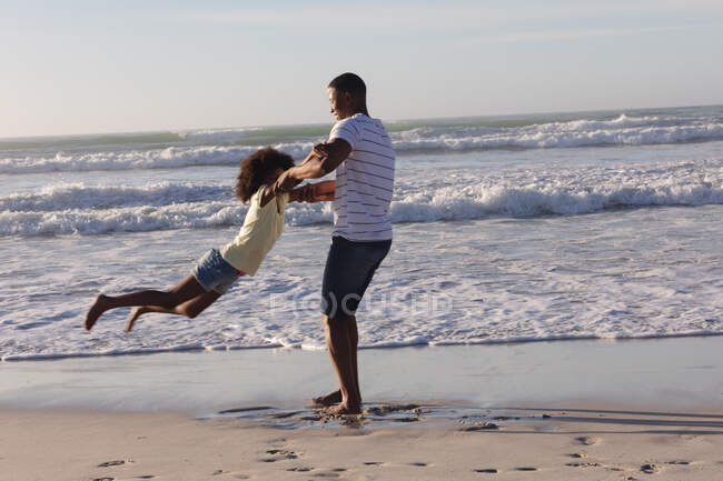 African american father and daughter having fun spinning at the beach. family outdoor leisure time by the sea. — Stock Photo