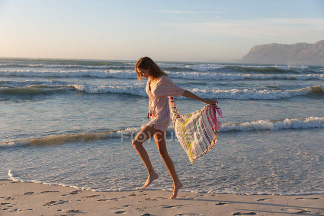 Bella donna caucasica tenendo sciarpa a piedi e godendo in spiaggia. estate concetto di vacanza al mare. — Foto stock