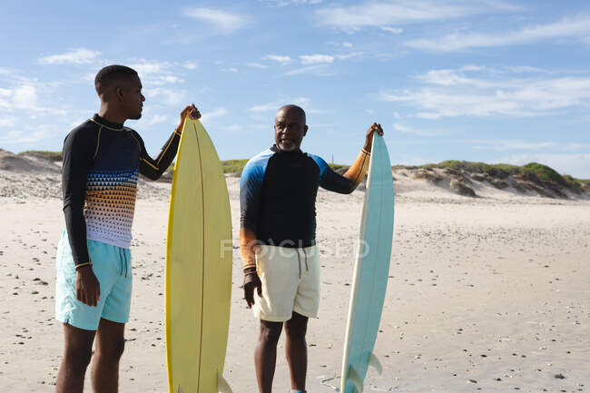 Африканський батько і син з дошками для серфінгу стоять на пляжі. Літні канікули та концепція дозвілля.. — стокове фото