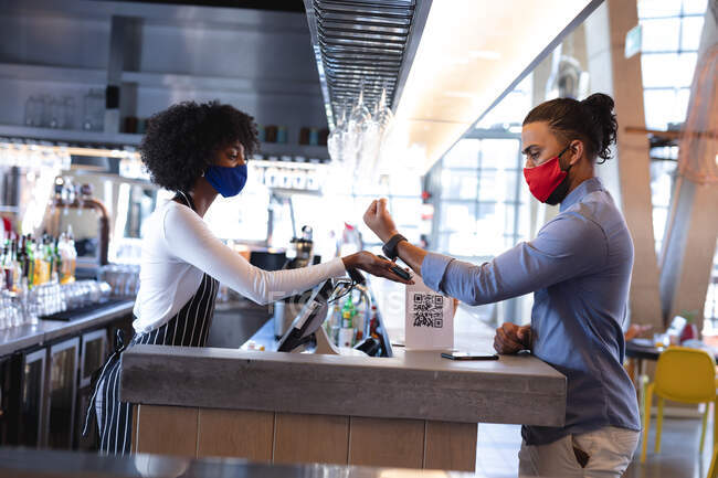 Різні чоловіки і жінки-офіціанти носять маску обличчя, використовуючи платіжний термінал у кафе. Незалежна кава, бізнес під час коронавірусної ковини 19 пандемії. — стокове фото