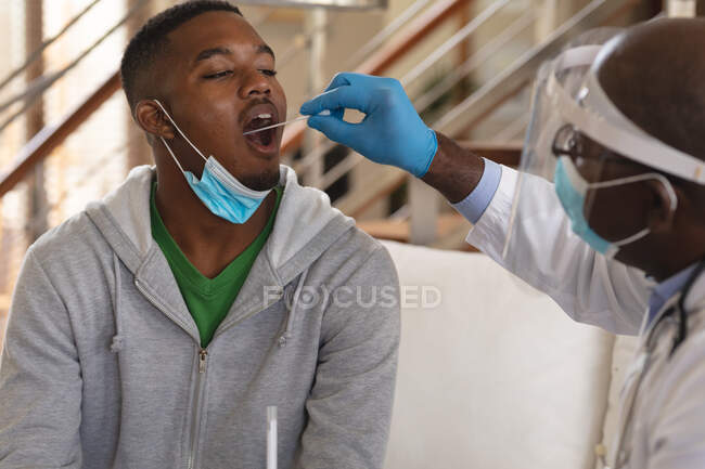 Афроамериканець, старший лікар чоловічої статі, робить аналіз горла на африканського американця вдома. Медичні тести для запобігання спалаху коронавірусу — стокове фото