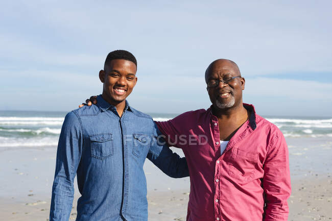 Портрет африканского американского отца и его сына, улыбающихся, стоя вместе на пляже. летний отдых на пляже и досуг. — стоковое фото