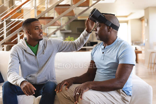 Jeune homme afro-américain enseignant à son père comment utiliser un casque vr à la maison. concept de technologie familiale et de divertissement — Photo de stock