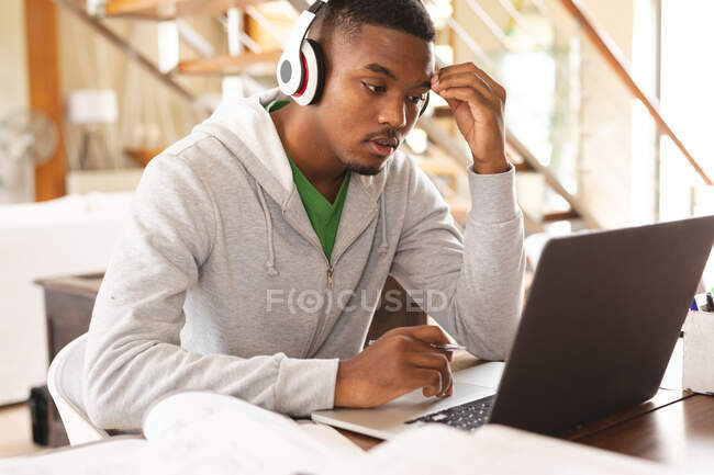 Hombre joven afroamericano estresado que usa auriculares con computadora portátil mientras estudia en casa. aprendizaje a distancia y concepto de educación en línea - foto de stock