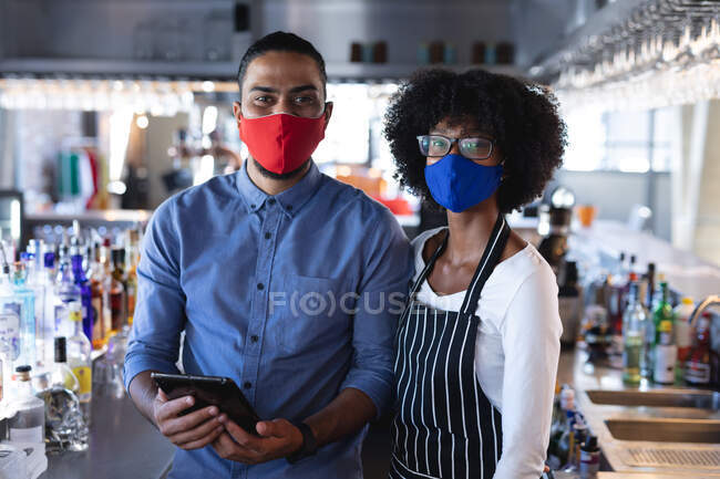 Diversos baristas masculinos y femeninos con máscaras faciales, mirando a la cámara. café independiente, negocio durante coronavirus covid 19 pandemia. - foto de stock