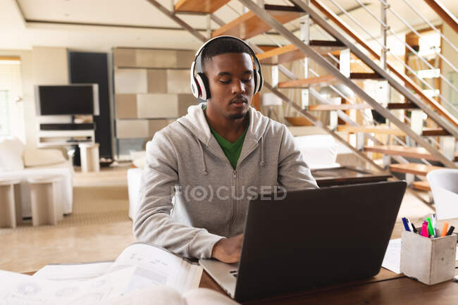 Afrikanischer junger Mann mit Kopfhörer und Laptop, während er zu Hause studiert. Fernstudium und Online-Bildungskonzept — Stockfoto