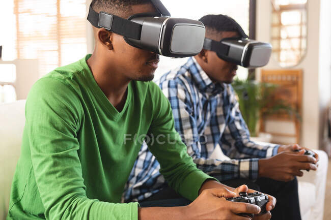 Irmãos afro-americanos vestindo fones de ouvido vr jogando videogames enquanto estavam sentados no sofá em casa. conceito de tecnologia de jogos e entretenimento — Fotografia de Stock