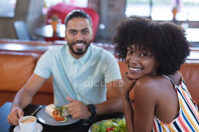 Улыбающийся мужчина смешанной расы и африканская американка, обедающая в ресторане. независимое кафе, небольшой успешный бизнес. — стоковое фото